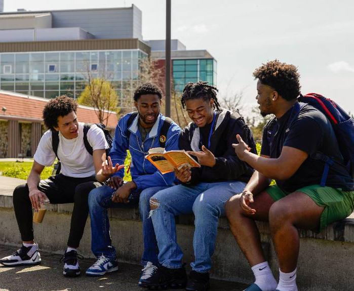 Four students sit in the campus commons and look at a book